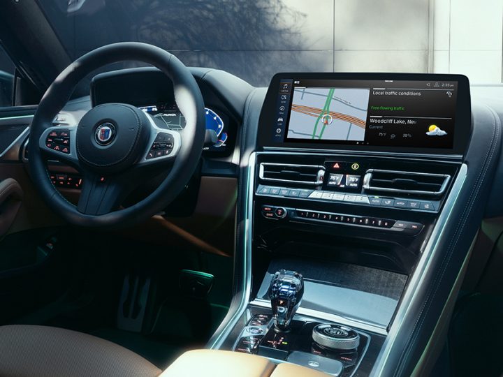 Cockpit view of a 2025 ALPINA B8 showing leather steering wheel, glass controls, and interior trim