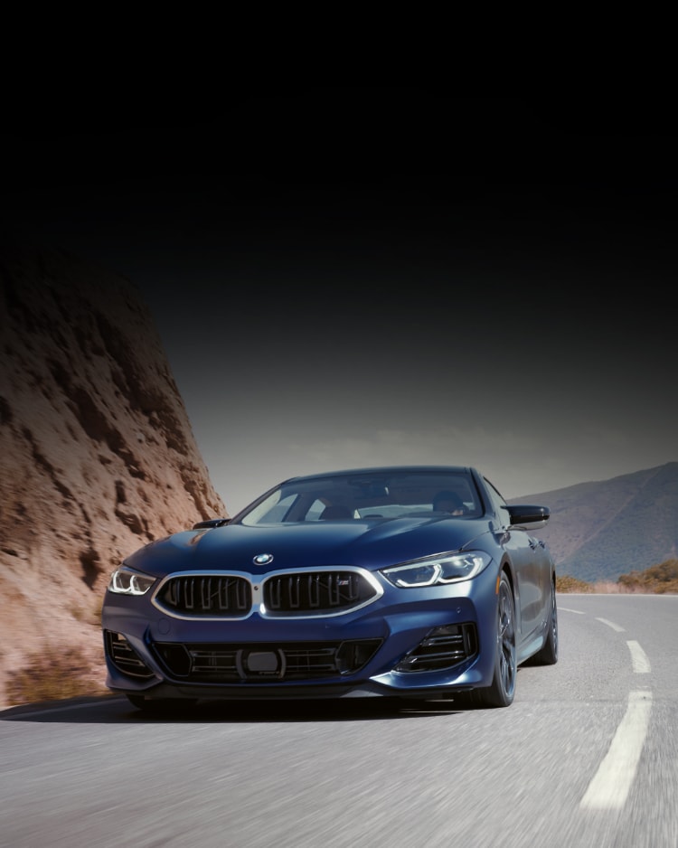 A 2026 BMW M850i xDrive Gran Coupe in Frozen Bluestone Metallic drives along a mountain road