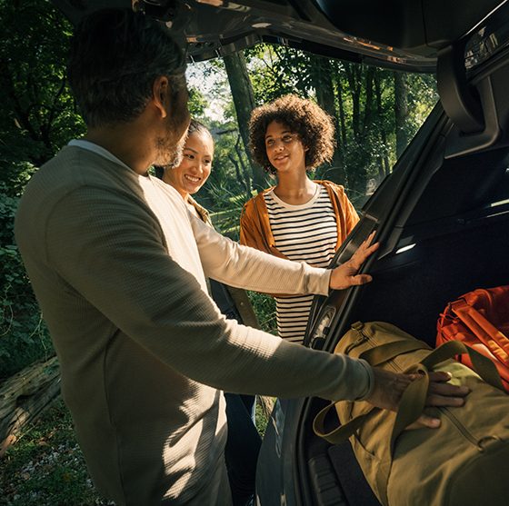 A family unpacking the trunk of their all-electric BMW after arriving at a forested vacation spot