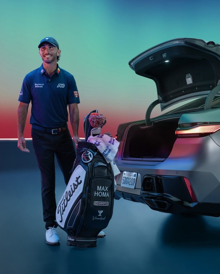 Max Homa smiles as he prepares to load his golf bag into the trunk of a BMW i7