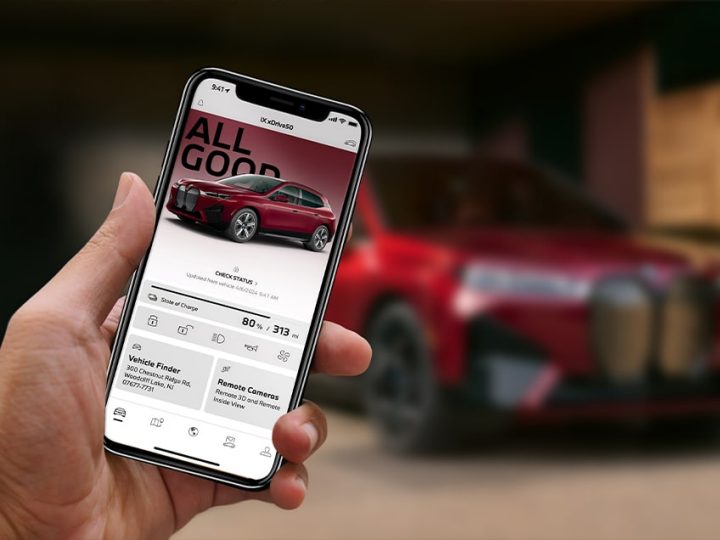 Detail of smartphone showing My BMW App in a person's hand with an iX xDrive50 in the intentionally blurred background
