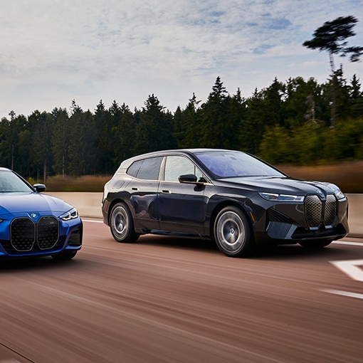 The 2025 BMX iX in motion, driving quickly down an HOV lane with evergreen trees in the background.