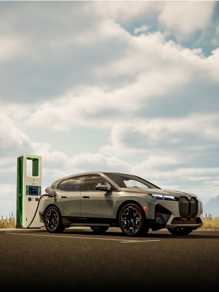 A BMW iX plugged into a charging station with mountains in the far distance.