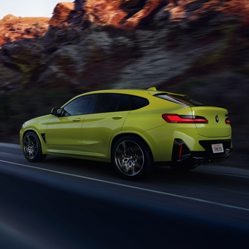 2025 BMW X4 M Performance Coupe SUV in Sao Paolo Yellow, accelerating down an open road