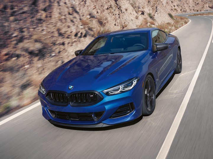 The 2026 BMW M850i xDrive in Portimao Blue Metallic driving down a scenic highway in front of a canyon background