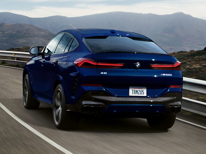 Rear view of 2026 BMW X6 M60i as it drives down a rural highway