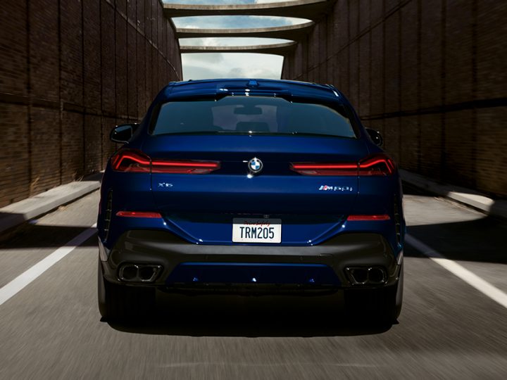 Rear view of 2026 BMW X6 M60i driving in an urban landscape