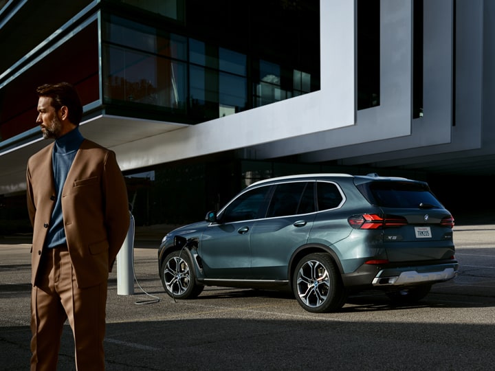 A sharp dressed man stands beside a charging BMW X5 PHEV without a care in the world